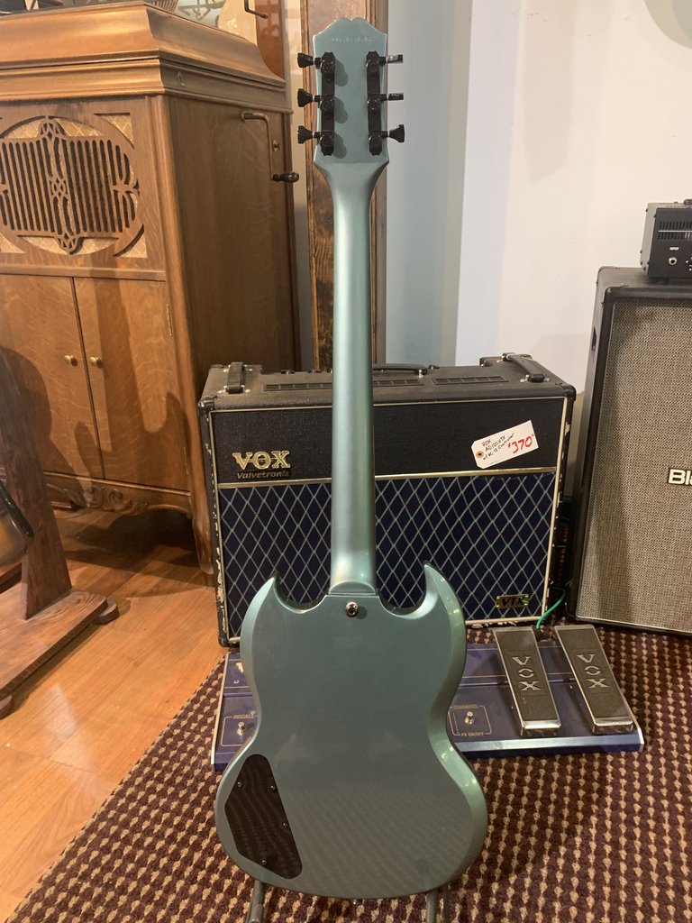 Back view of the metallic blue-grey Epiphone SG Special electric guitar, showing the solid body finish, set neck, and control cavity cover. The guitar is positioned in front of a Vox amplifier.
